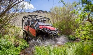 Four riders having fun whizzing down rocky trail in red Pioneer 1000-5 EPS equipped with hard roof and durable steel front bumper