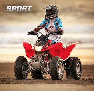 "A solid transitional ATV with an outstanding transmission." - Quote by ATV.com. Image of determined rider wearing ATV sport suit speeding up a dusty, dirt incline on red ATV.