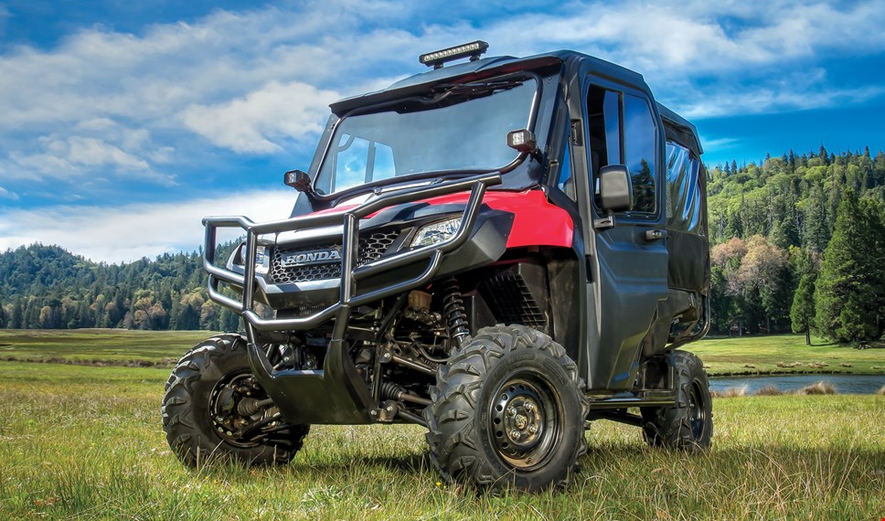 The red Pioneer 700-4 dressed up with durable hard front doors, glass windshield and mounted light bar and auxilary lights, parked in scenic forest meadow