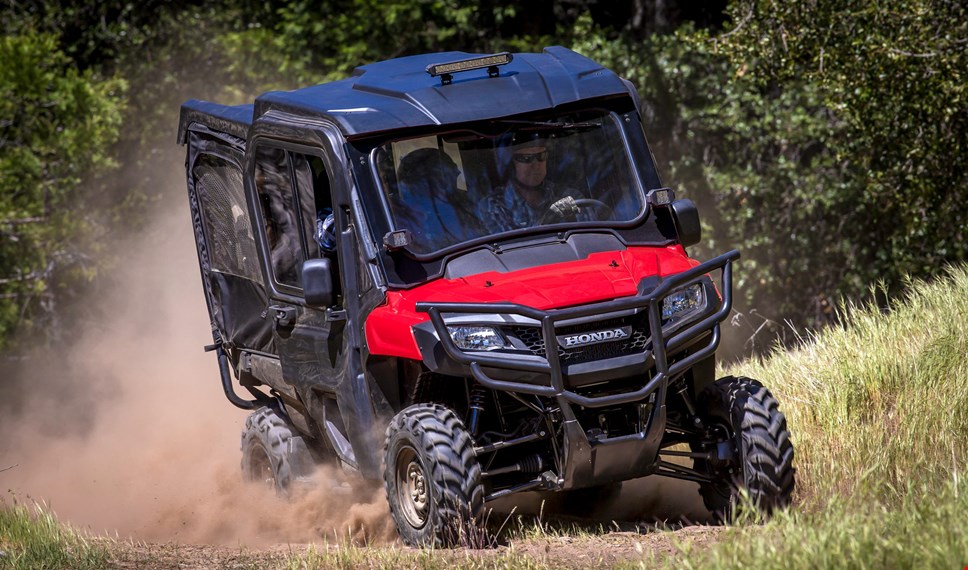 The red Pioneer 700-4 equipped with hard roof, glass windshield and fabric front doors cruising effortlessly over rugged dusty terrain