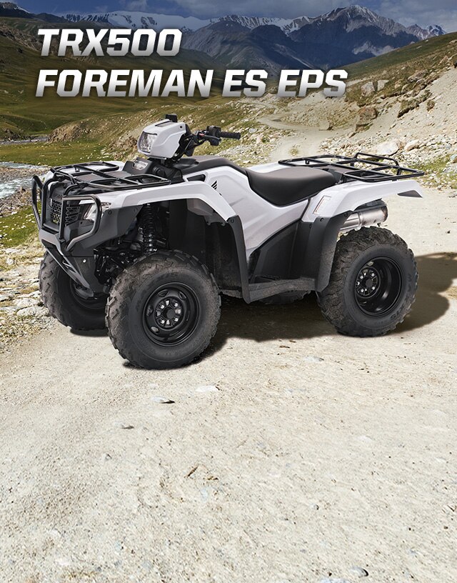 TRX500 Foreman ES EPS. La légende sans limite. Image d'un VTT orange stationné sur une piste de gravier avec des montagnes majestueuses en arrière-plan.