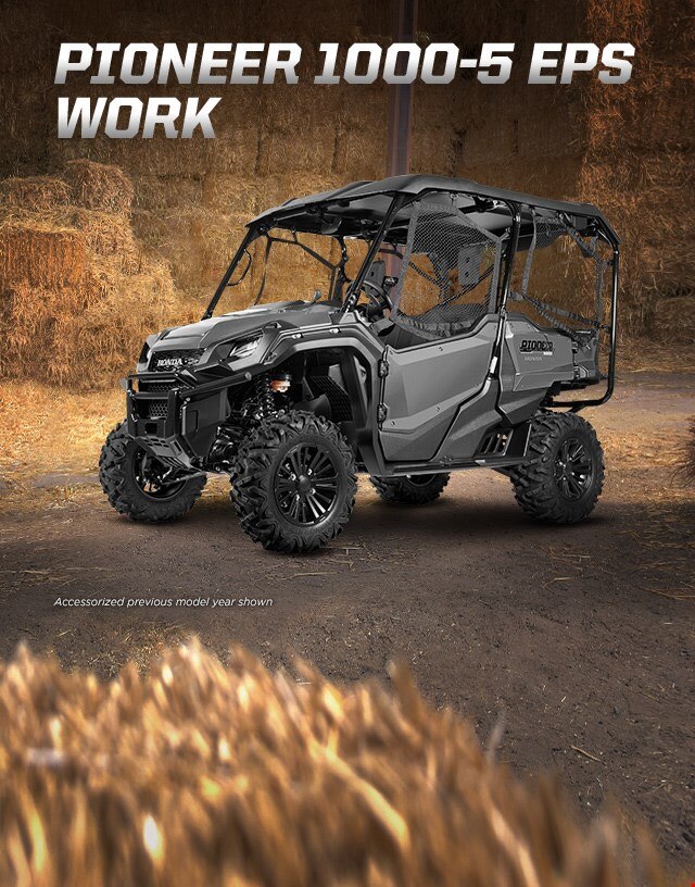 Pioneer 1000-5 EPS Work. Go beyond extraordinary. Black 5-person side-by-side with hard roof and roll-up side nets parked in hay barn