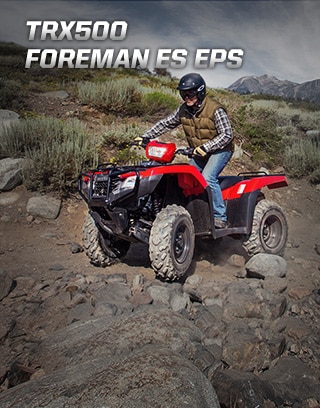 TRX500 Foreman ES EPS. The limitless legend. Image of orange ATV dramatically parked on gravel trail with majestic mountain peaks in background.