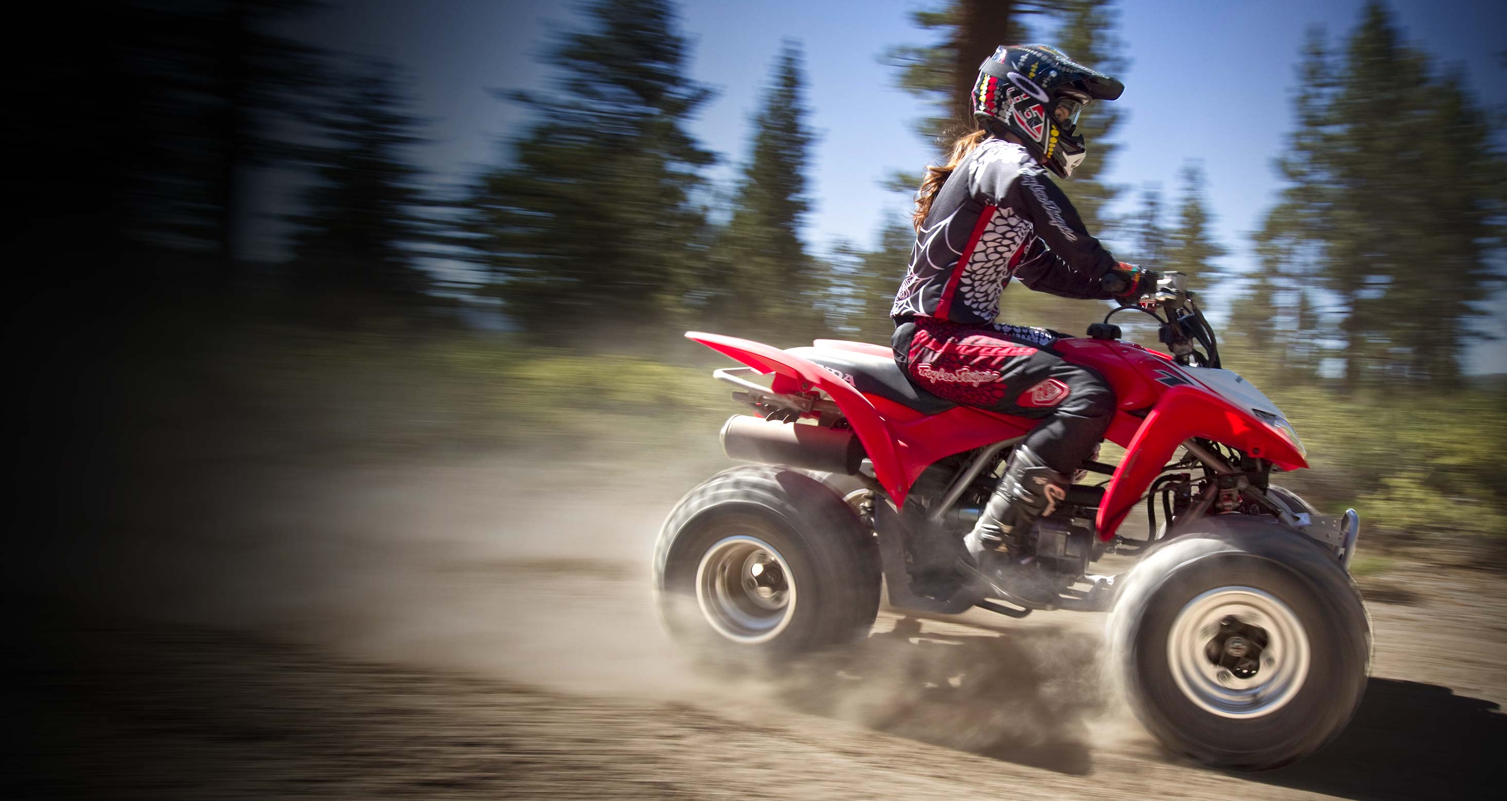 Image of girl riding a red TRX250 ATV on a dirt road