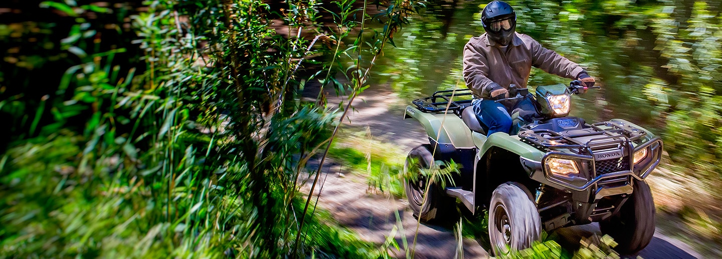 ATV rider on trail accelerating through lush green shrubbery
